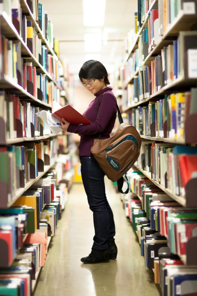 Student immersed in study at the library, surrounded by books, embodying the pursuit of knowledge and academic diligence.